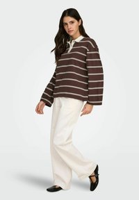 Pruunide ja valgete triipudega piklike varrukatega pluus kraega kaelusega, kombineeritud laia valge pükstega ja mustade ümarate tasaste kingadega.