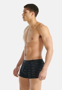 Czarne bokserki z geometrycznym wzorem, wykonane ze streczowej tkaniny, z szerokim, elastycznym pasem; model pokazany z boku.