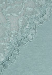 Jasnoniebieska tkanina z teksturową koronką w kwiatowe wzory i falbaniastymi brzegami. Materiał bazowy jest gładki i elastyczny.
