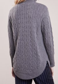 Suéter gris de punto con patrón de trenzas, cuello alto y dobladillo acanalado. Presenta aberturas laterales y un bajo redondeado para mayor comodidad.