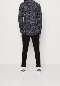 Navy paita valkoisella lehtikuviolla, pitkät hihat ja kaulus; yhdistetty mustiin housuihin ja valkoisiin lenkkareihin, joissa on mustat yksityiskohdat.