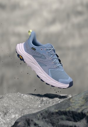 Scarpe da corsa azzurro chiaro con tomaia in mesh e dettagli testurizzati, con una suola intermedia bianca spessa e dettagli viola sulla suola esterna. Linguetta posteriore gialla.