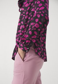 Musta paita, jossa on vaaleanpunainen huulipaino, pitkät hihat nappikannella, yhdistetty vaaleanpunaisiin housuihin, jotka esittelevät sileää rakennetta ja istuvaa muotoilua.