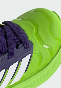 Bright green athletic shoe featuring a textured rubber sole with zigzag patterns, purple laces, and white accents on the side.