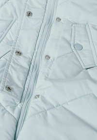 Lichtblauwe gewatteerde jas met frontzipper en drukknoopjes, voorzien van klepzakken die zijn beveiligd met ronde drukknoopjes.
