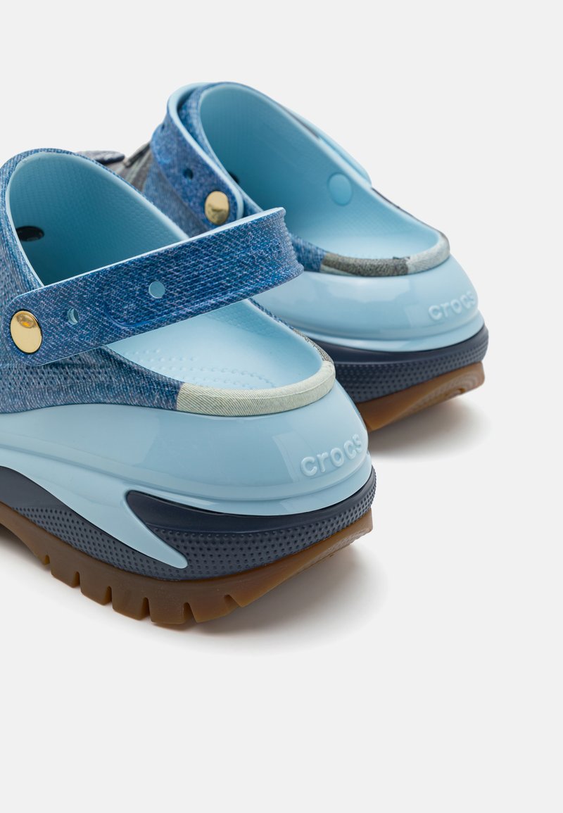 Zuecos de color azul y textura de denim con correas ajustables, un acabado brillante y una suela antideslizante, que presentan un logotipo en la parte trasera.