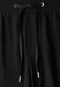 Pantalons de survêtement noirs avec une taille élastique, dotés d'un cordon de serrage avec des embouts en métal argenté et d'une texture de tissu lisse.