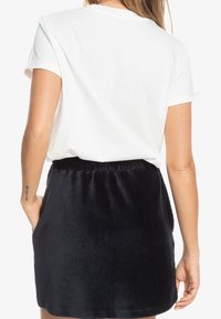 Weißes Baumwoll-T-Shirt mit aufgerollten Ärmeln, kombiniert mit einem schwarzen Samtrock mit Taschen und einem elastischen Bund.