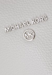 Superficie in pelle bianca testurizzata con lettering metallico "MICHAEL KORS" e un logo circolare "MK", che mostra un design elegante.