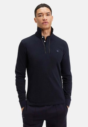 Polo à manches longues bleu marine avec un col haut, patte de boutonnage et un petit logo en accent. Texture lisse, design ajusté.