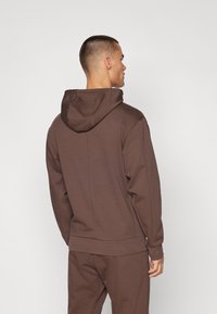Sweatshirt castanho com capuz ajustável, punhos e margem canelados. Textura de tecido suave com um corte clássico, visto de costas.