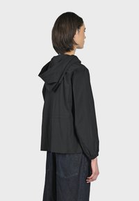 Giubbotto nero con cappuccio, con polsini elasticizzati e vestibilità ampia, caratterizzato da una texture liscia e opaca e da un design semplice e minimalista.