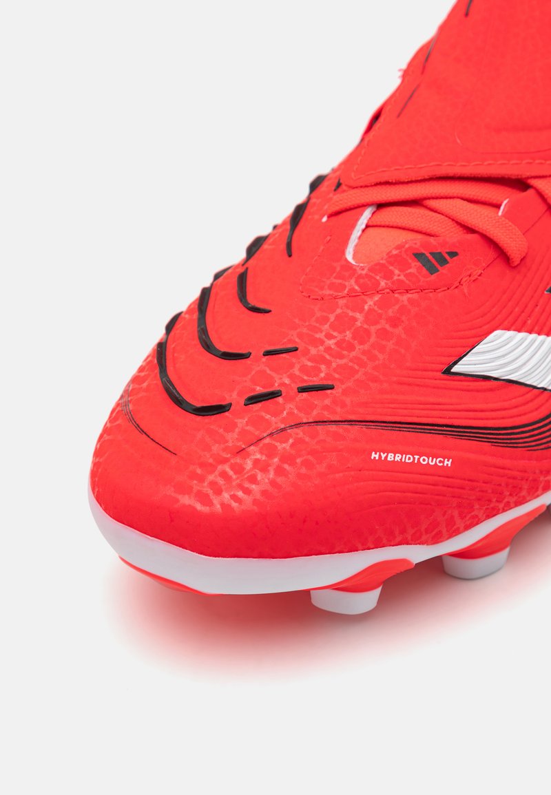 Bottine de football rouge en matériau synthétique texturé, avec des accents noirs et blancs, un motif distinctif en écailles, et un design courbé.