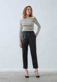 Top de hombros descubiertos a rayas en crema y negro con mangas largas, combinado con joggers de piel negra de cintura alta que cuentan con una banda elástica.