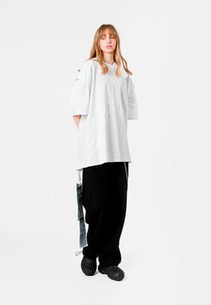Camiseta blanca de gran tamaño con aberturas laterales, pantalones de pierna ancha negros y zapatos chunky negros con suela texturizada.
