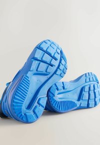 Blå sportskor med texturerade gummisulor, som har ett mönstrat grepp för fäste och en konturerad design för komfort.