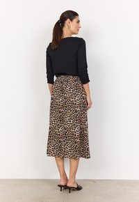Haut noir à manches longues associé à une jupe imprimé léopard arrivant au genou. La jupe a une taille élastique et un design fluide. Mules à talons noirs.