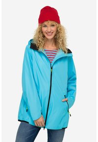 Giacca antipioggia azzurro chiaro con cappuccio nero, zip anteriore e tasche a filetto. Caratterizzata da una texture liscia e una vestibilità casual, abbinata a un berretto rosso.
