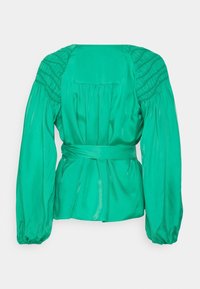 Blouse en satin vert avec manches bouffantes, épaules smockées, taille nouée et dos fluide avec un pli. Texture lisse sur toute la surface.