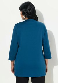 Teal tunika i stil med mjukt tyg, med trekvartslånga ärmar och rundad halsringning. Enkelt design utan synliga mönster.