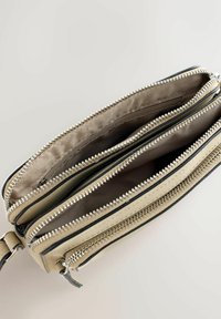 Beige skuldertaske med to åbne rum med lynlås og en ekstra lomme med lynlås foran, der viser stofforet indeni.