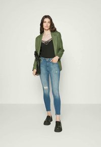 Zeleni karirani sako preko črne bluze s čipkastim robom, v kombinaciji z raztrganimi modrimi skinny jeans hlačami in črnimi platform čevlji.