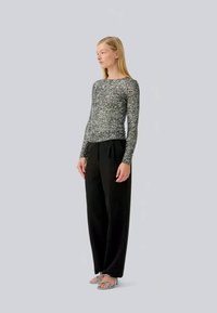 Langärmeliges, eng anliegendes Oberteil aus schwarz-weißer gesprenkelter Strickware, kombiniert mit lockeren schwarzen Hosen. Das Modell trägt silberne Sandalen. Minimalistisches Design.