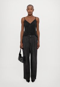 Top negro sin mangas con lunares blancos, diseño de escote en forma de V, combinado con pantalones holgados negros y un bolso negro. Los tacones completan el conjunto.