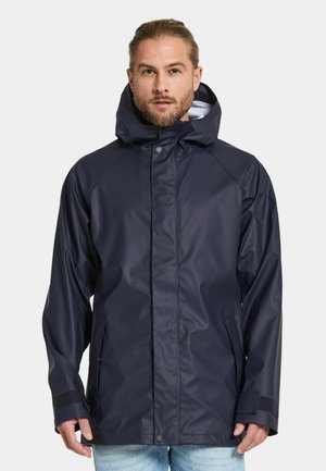 Marineblå vandtæt jakke med hætte, med en frontlynlås, trykknaplukning, sidelommer og teksturerede manchetter. Glat, shiny finish.