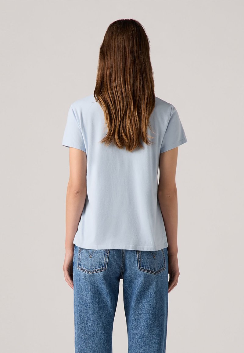 Camiseta de manga corta azul claro con escote redondo, hecha de algodón suave. Combinada con unos vaqueros de mezclilla azul claro que cuentan con bolsillos traseros.
