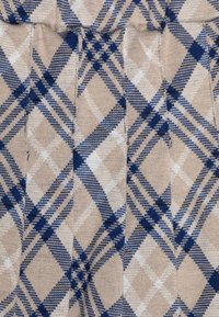 Tessuto beige con un motivo a quadri blu e bianco caratterizzato da linee incrociate e diamanti. La texture appare morbida e lavorata a maglia.