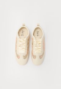 Baskets beige avec des accents en tissu ornés de broderies florales, lacets plats et une boucle au talon pour un enfilage facile. Matériau synthétique lisse.