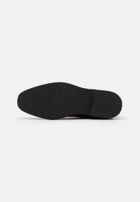 Semelle de chaussure noire avec une surface texturée. La forme est légèrement incurvée, avec un bord lisse et sans marque ni motif visible.