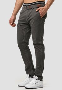 Pantalones ajustados grises con un patrón a cuadros, que cuentan con una cinturilla a rayas en blanco y negro y detalles en cuero marrón, combinados con zapatillas blancas.
