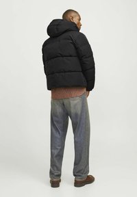 Sort dunjakke med hætte, med et quiltet design. Båret over en rød plaidskjorte og løstsiddende blå jeans, kombineret med brune sko.