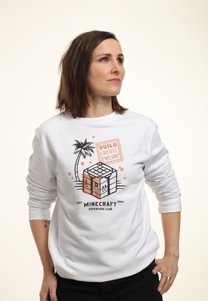 Biała bluza z grafiką Minecraft, przedstawiającą pikselowy blok i palmę, z pomarańczowym i czarnym napisem, na neutralnym tle.