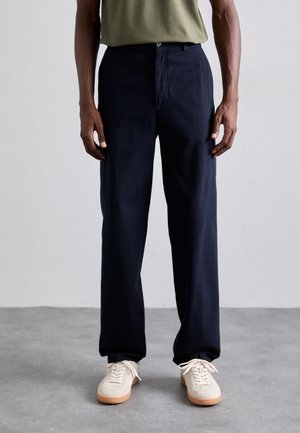 Navy blue wide-leg trousers made of cotton fabric with front pockets and a zip fly, paired with light-colored sneakers.