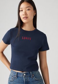 Temno modra bombažna majica s kratkimi rokavi, sredi prsi z rdečim napisom "LEVI'S". Preprost dizajn, skrajšan kroj, gladka tekstura.