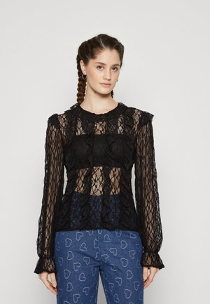 Top nero in pizzo a maniche lunghe con dettagli arruffati e sezioni trasparenti. La texture a fantasia contrasta con il tessuto solido sottostante.
