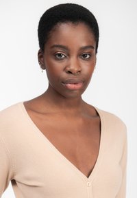 Beige V-Ausschnitt-Pullover mit strukturiertem Finish, ausgestattet mit einem einzigen Knopfverschluss vorne und einer enganliegenden Silhouette.