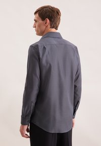 Camicia a maniche lunghe di colore blu scuro con un piccolo motivo a scacchi, polsini con bottoni e colletto a punta. Tessuto liscio con una vestibilità su misura.