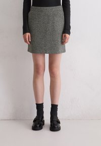 Grauer Woll-Minirock mit einem schlichten Design, der bis zur Mitte des Oberschenkels reicht, kombiniert mit schwarzen Loafers und dunklen, gerippten Socken.