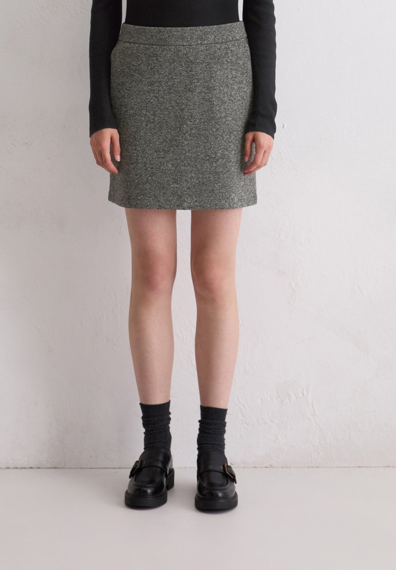 Grauer Woll-Minirock mit einem schlichten Design, der bis zur Mitte des Oberschenkels reicht, kombiniert mit schwarzen Loafers und dunklen, gerippten Socken.