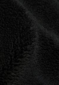Gros plan sur un tissu polaire noir doux présentant une surface texturée, duveteuse avec des fibres fines et des plis délicats.