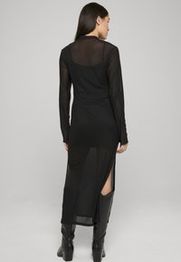 Robe noire à manches longues avec une texture transparente, une fente haute et une coupe ajustée. Comprend une doublure noire unie avec des accents minimalistes et une coupe sur mesure.