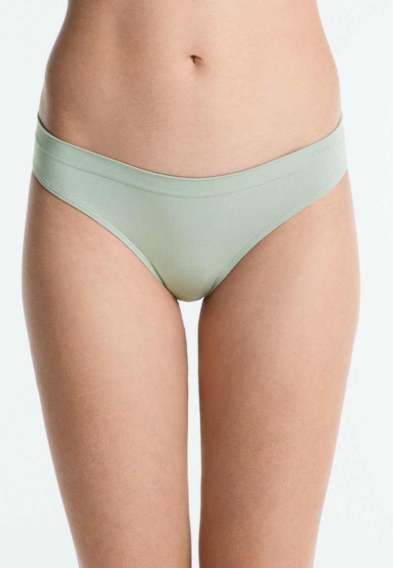 Gros plan d'une personne portant un sous-vêtement style bikini sans coutures vert clair, montrant le bas de l'abdomen et le haut des cuisses.