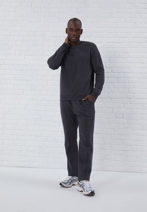 Sudadera gris oscuro y pantalones a juego de tejido suave, con un corte relajado, puños acanalados y bolsillos laterales. Zapatillas plateadas complementan el conjunto.