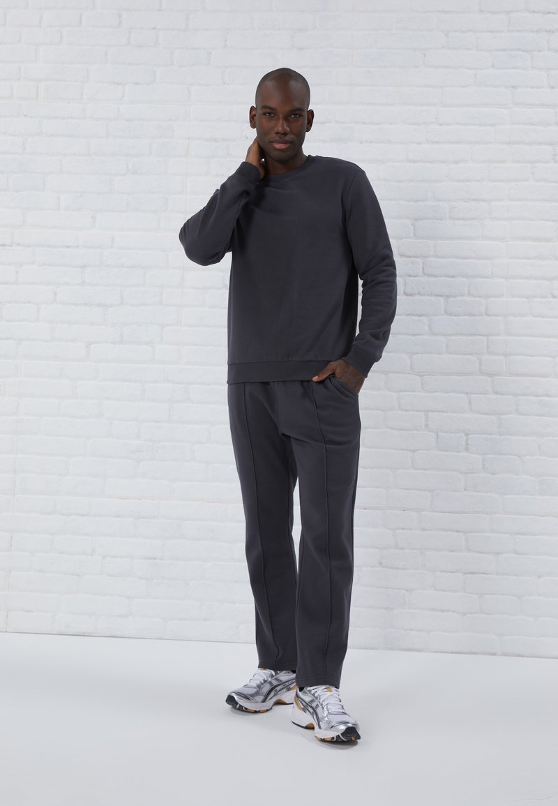Dunkelgrauer Sweatshirt und passende Hose aus weichem Material, mit legerem Schnitt, gerippten Bündchen und Seitentaschen. Silberne Sneaker runden den Look ab.