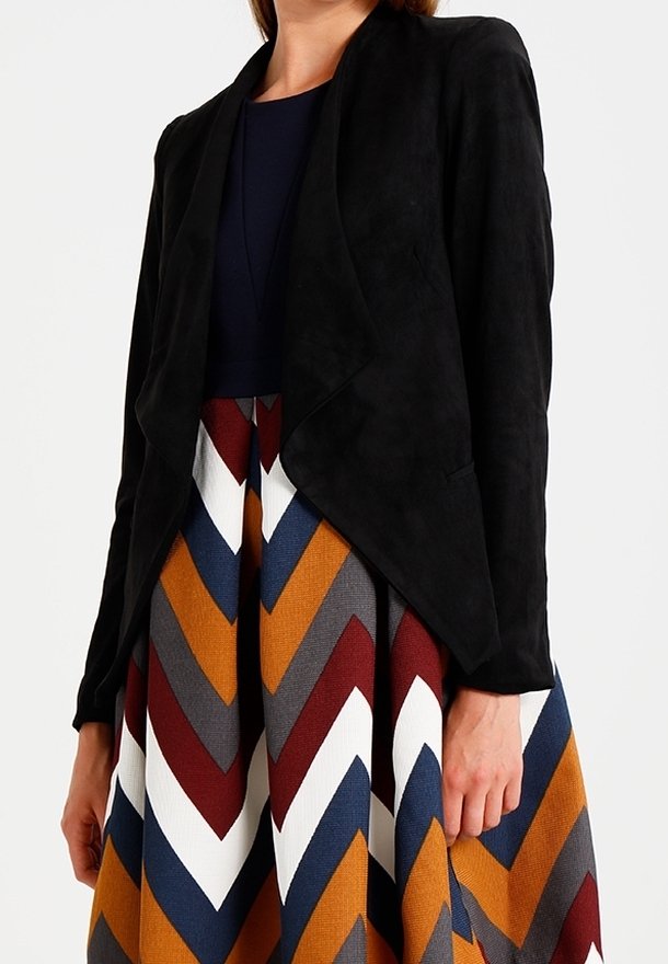 Mujer con chaqueta negra abierta sobre una falda con estampado de chevron multicolor en azul marino, óxido, gris, blanco y burdeos.