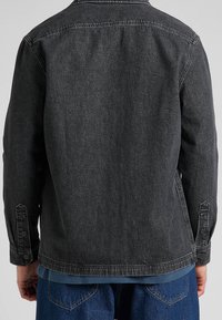 Černá džínová bunda s volným střihem, dlouhými rukávy, knoflíkovými manžetami a špičatým límcem. Má lehce vybledlou texturu a detaily šití.